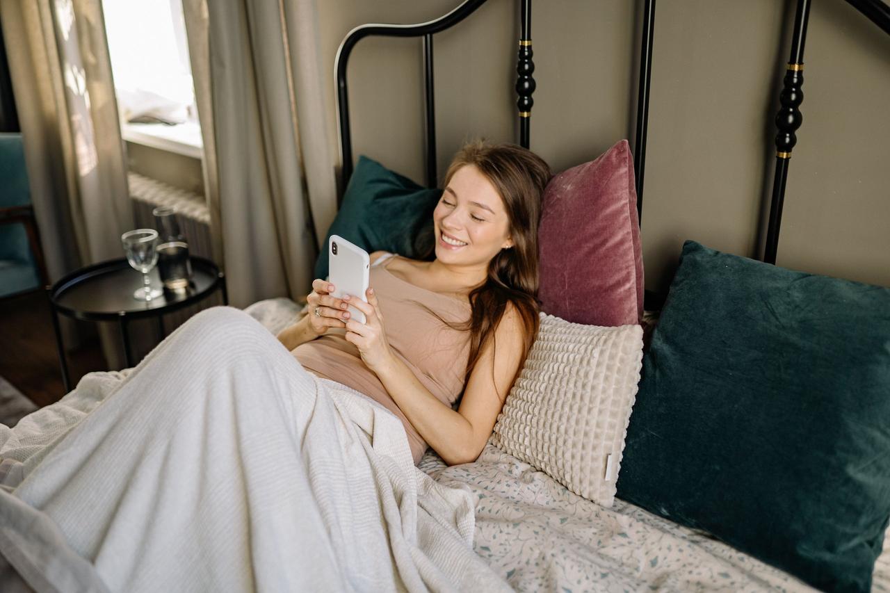 woman in bed smiling at phone
