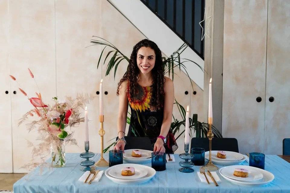 A smiling wedding planner poses by a dressed table with dinner candles, plants and flowers