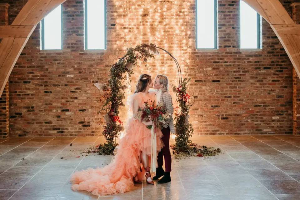 two brides standing in front of a floral wedding arch and fairy lights in a winter wedding venue