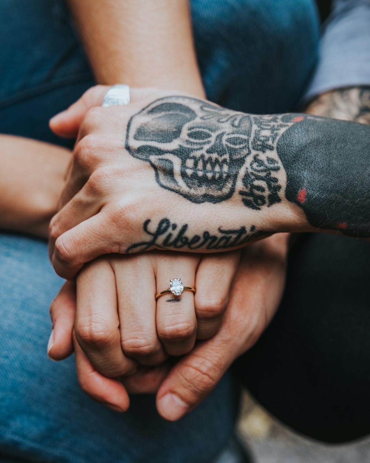 Couple holding hands showcasing tattoos and a woman's engagement ring