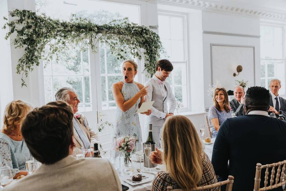 Bride, groom and wedding guests laughing at a wedding speech