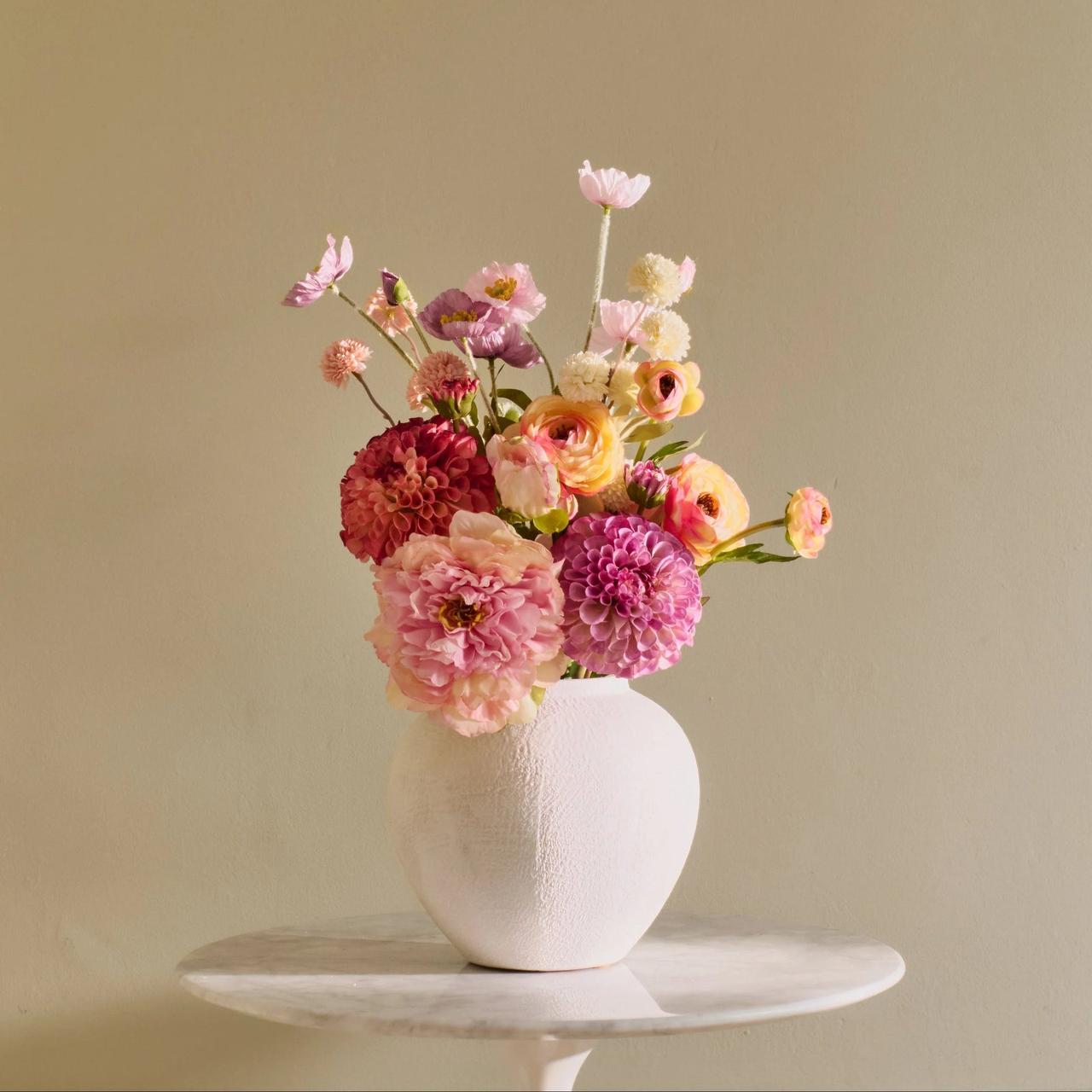 An array of peach and pink coloured flowers arranged in a white vase.