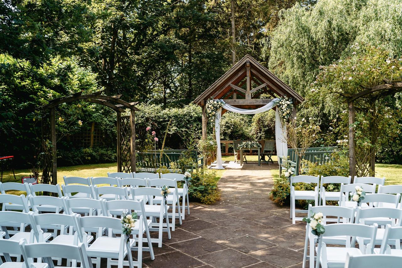 An outdoor ceremony set up with a woodland backdrop and white chairs.
