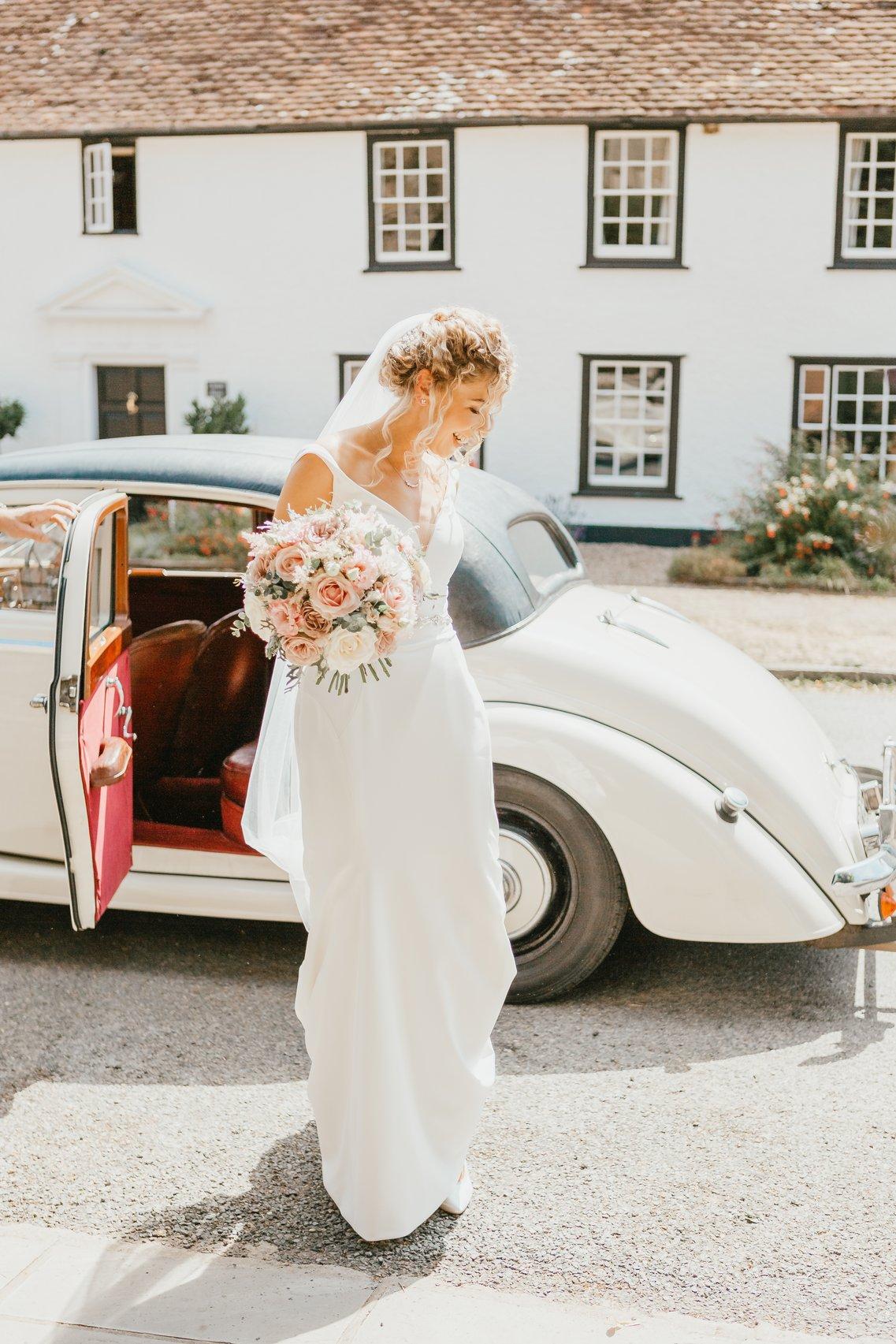The bride steps out of the wedding car with her blush pink bouquet
