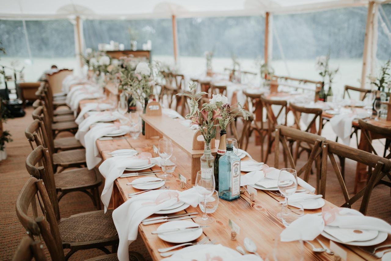 a bohemian, decorated long wedding table in a marquee within a woodland wedding venue with wooden chairs either side