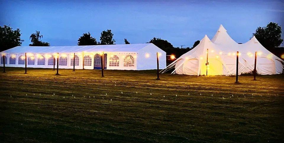 Tipi and marquee wedding venue at dusk lit up by warm lights