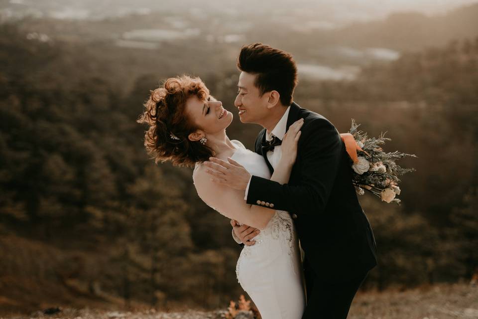 A bride and groom embracing and laughing at the top of a hill