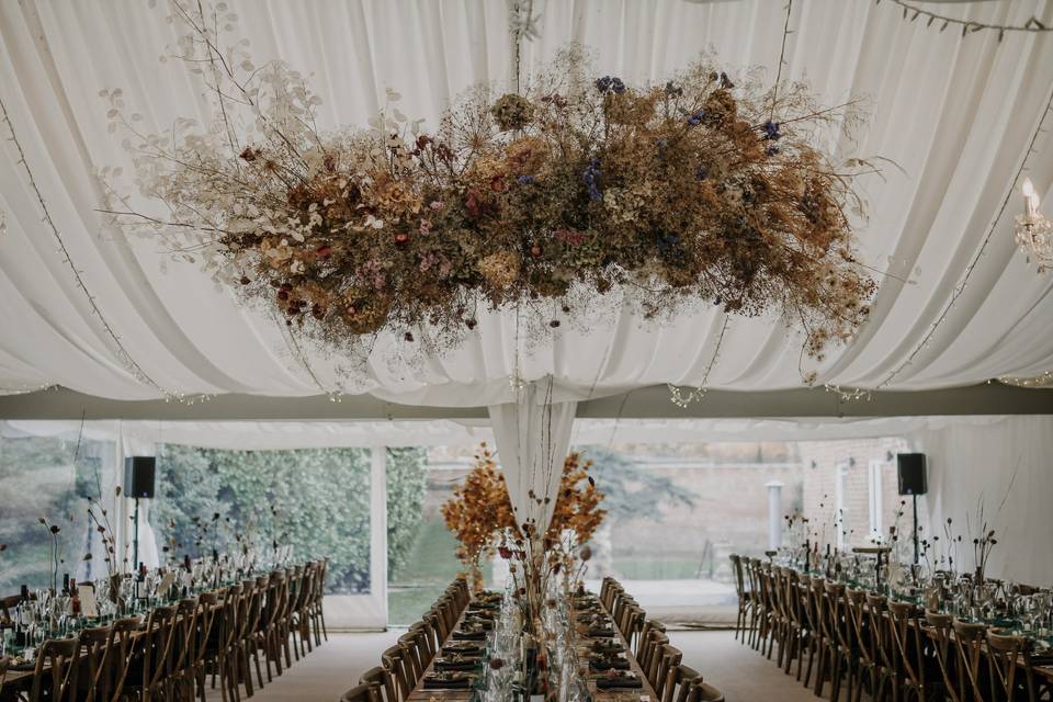 Marquee interior of Garthmyl Hall with rows of tables and a huge floral chandelier hanging from the ceiling.