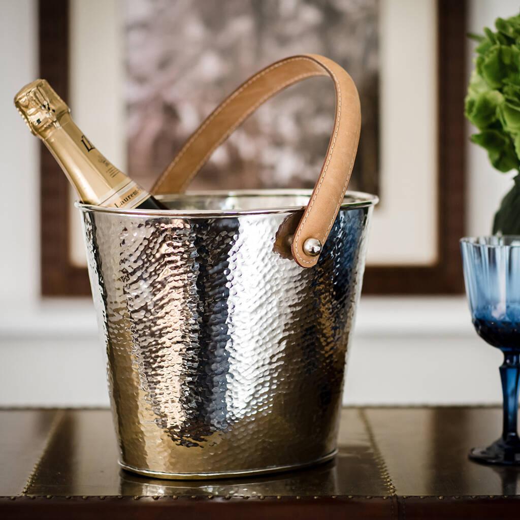 A silver hammered metal champagne cooler with a leather handle on a table.