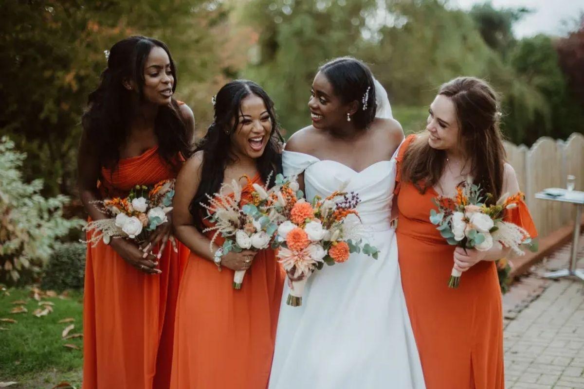 a bride posing with her three bridesmaids who are all wearing orange bridesmaid dresse which match the colours of the white and orange bouquets