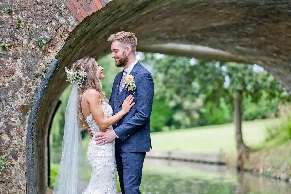 bride and groom embrace under a bridge by a river