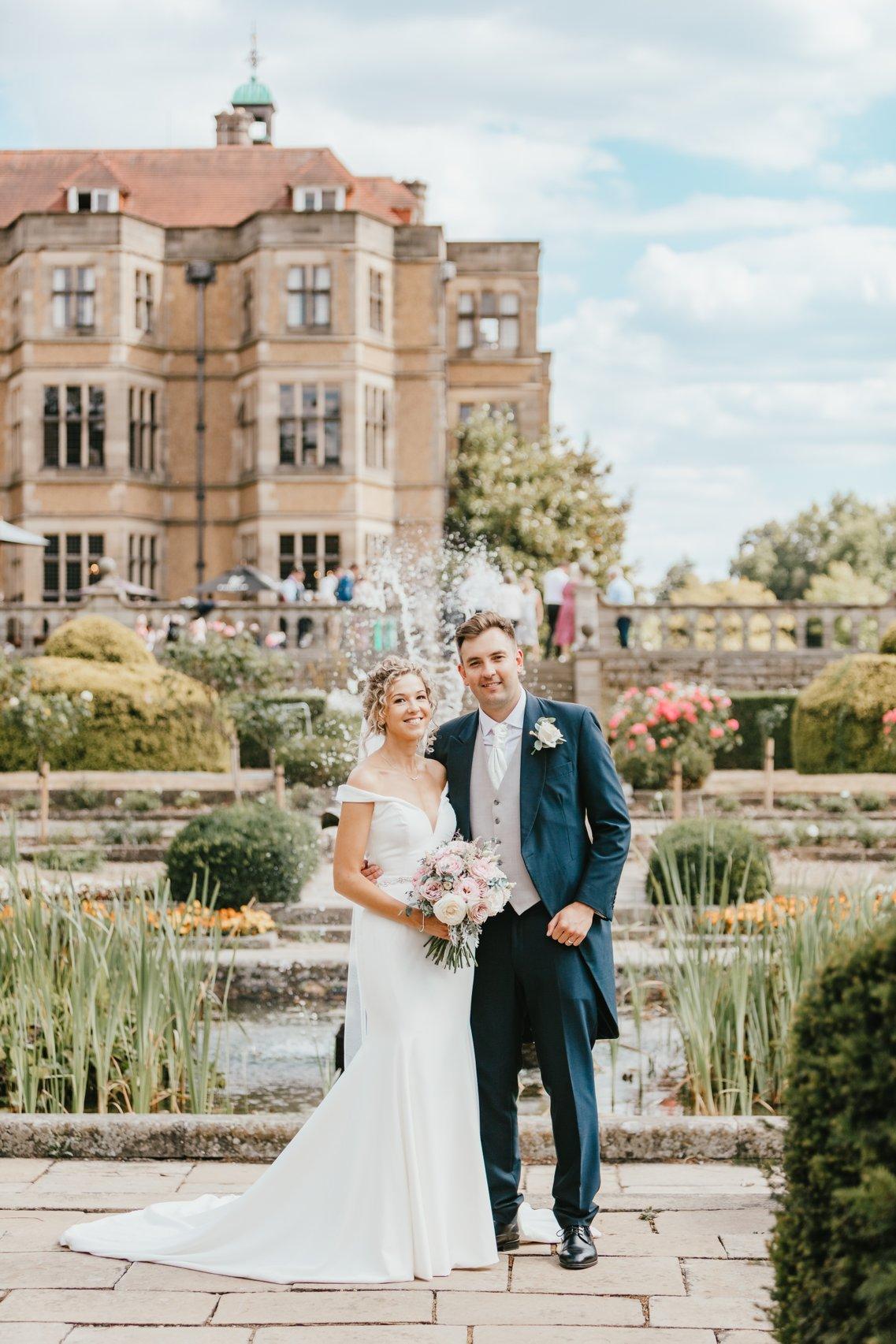 The bride and groom pose in front of the fountain and gardens at Fanhams Hall