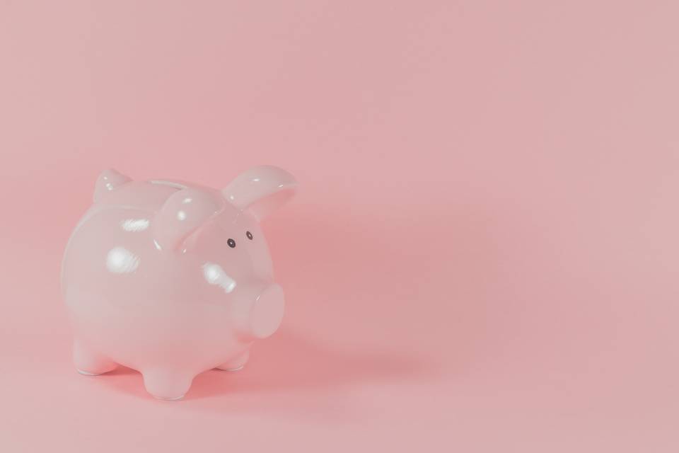 A pink china piggy bank with a small hole for coins on a pink background
