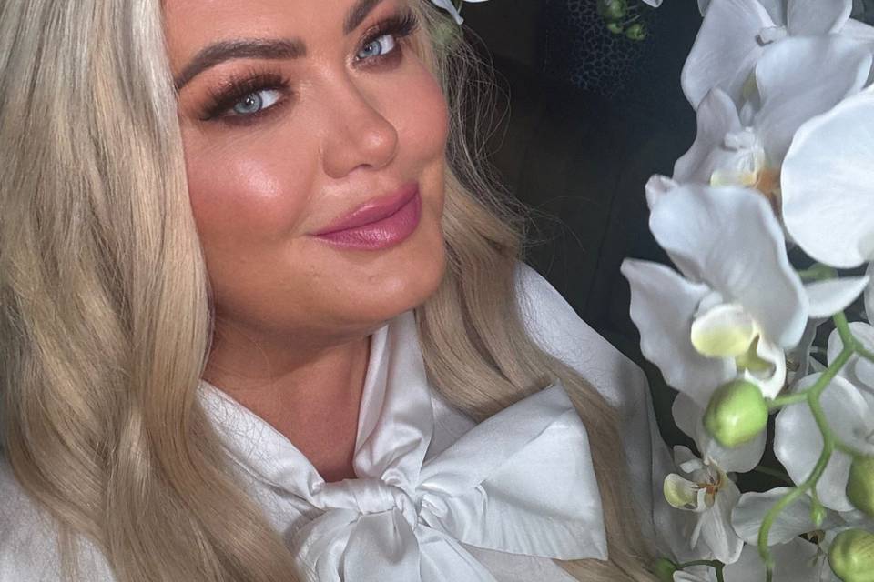 Gemma Collins wearing a wedding white top posing next to a white orchid plant