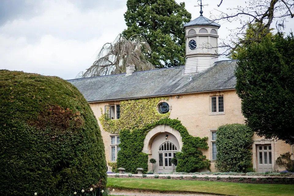 Building exterior with a clock tower, climbigng ivy, lawns and hedges 