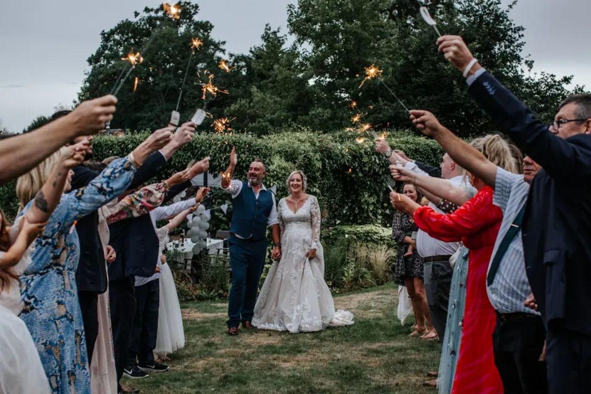 wedding guests holding sparklers to create an arch for a bride and groom to walk through after their daytime wedding