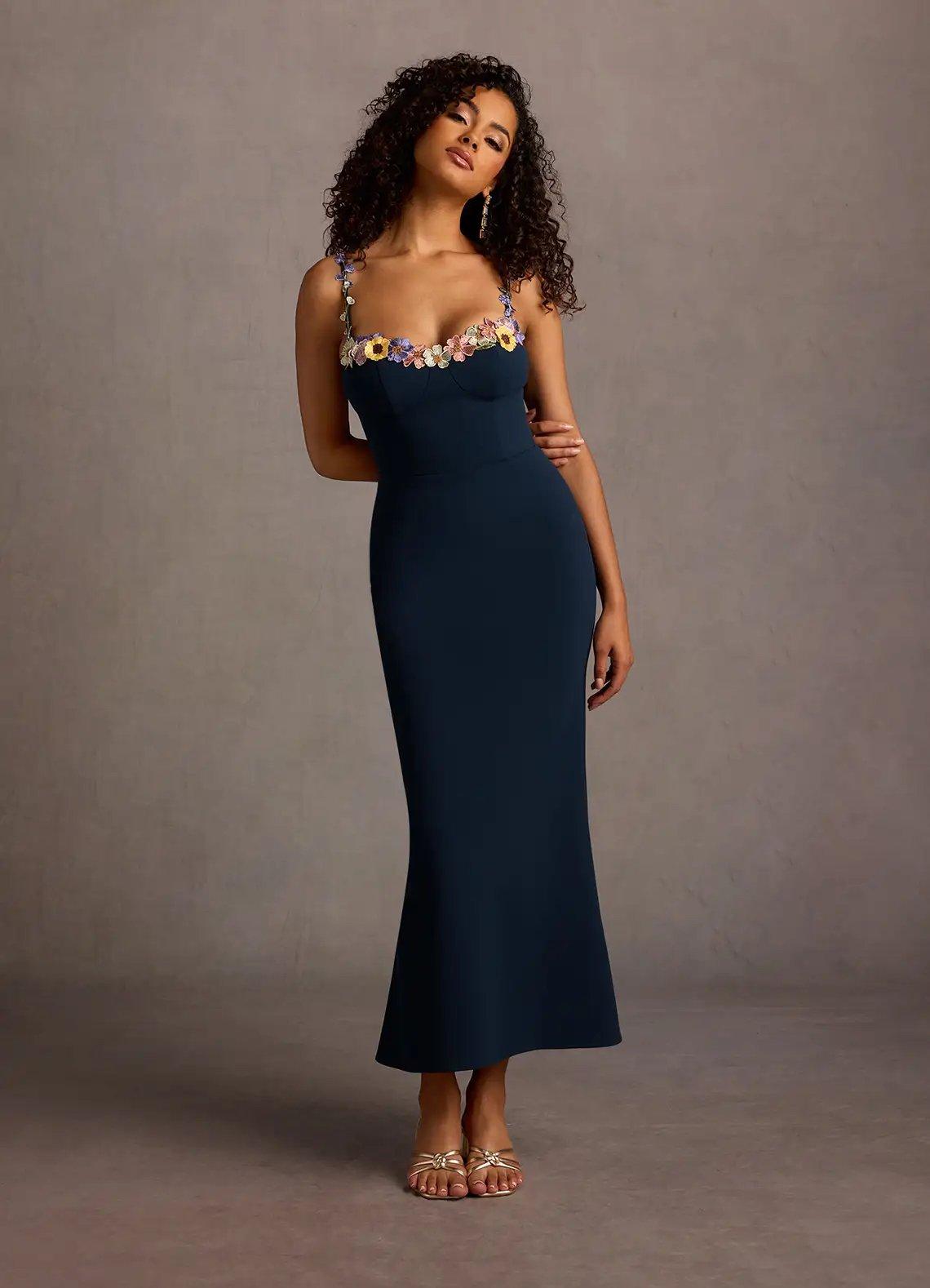 a wedding guest wearing a navy blue midaxi dress with colourful floral embroidery around the neckline and on the spaghetti straps.