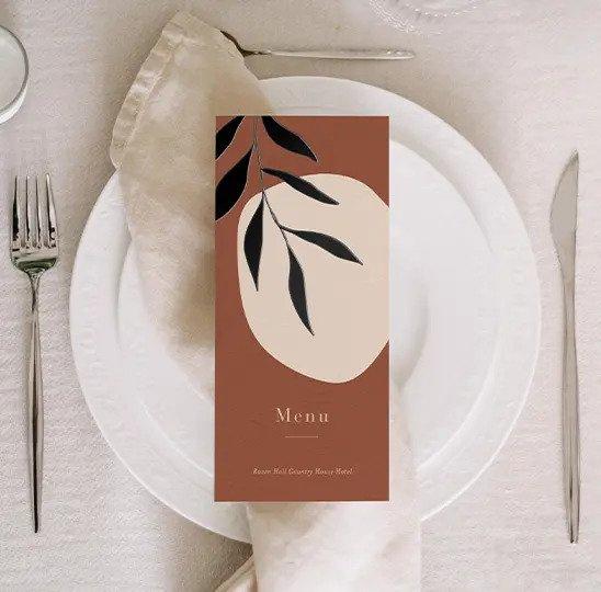 Sunset brown menu with black leaves placed on a plate beside a knife and fork#