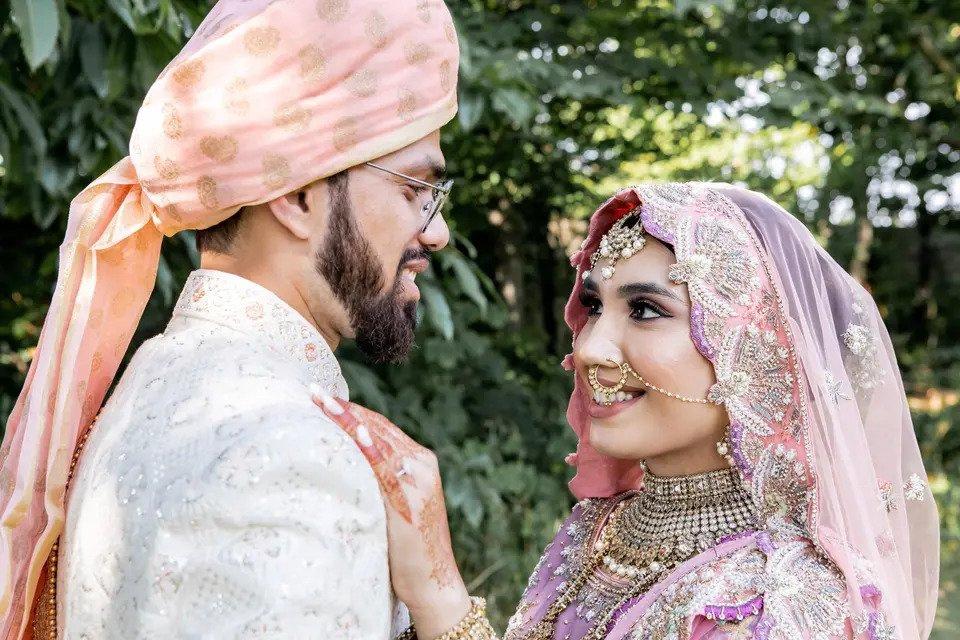 Asian bride and groom in traditional wedding clothes looking at each other and smiling