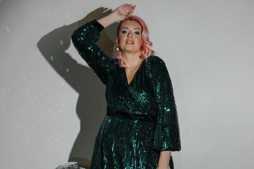 mother of the bride with pink hair standing against a white wall in a green sequin plus size mother of the bride dress