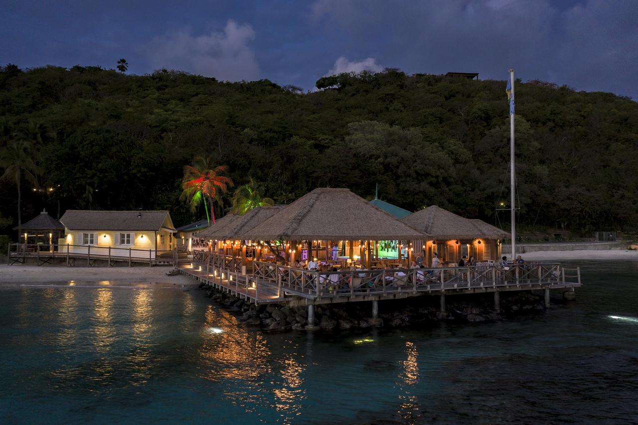 Basil Bar, Mustique is an infamous party spot for celebrities and great for cocktails and partying. Shot of the bar at night time, a tikki-style restaurant in the middle of the clear ocean