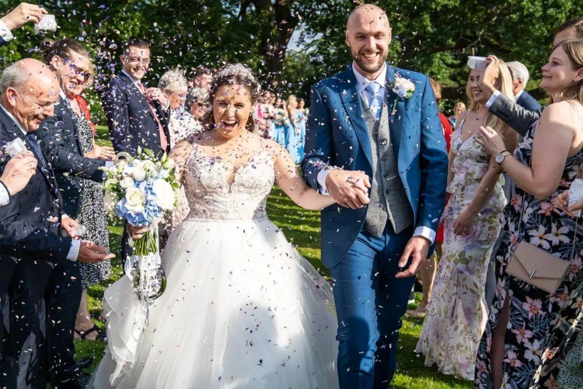 a bride and groom walking hand in hand as guests throw colourful confetti over them