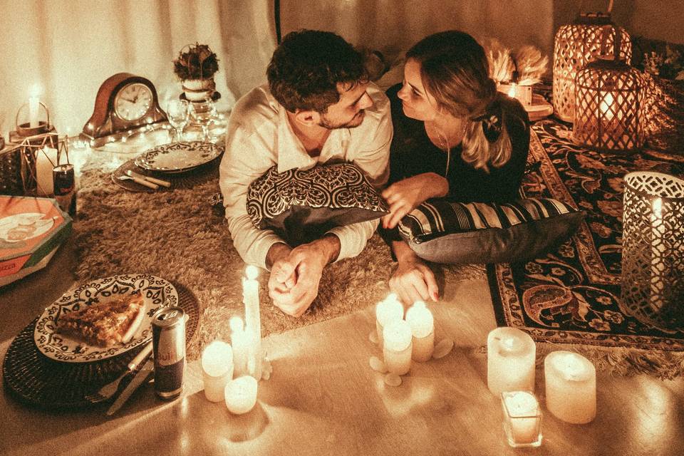 a couple enjoying a date night at home lying on rugs with candles and snacks around them