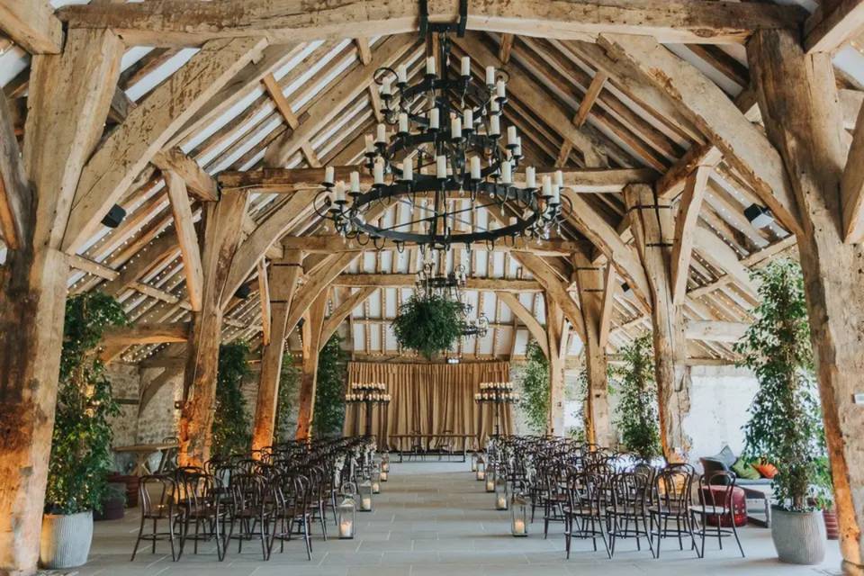 A high ceiling wooden beam barn with a candle-lit aisle and dark wooden chairs set up for a ceremony