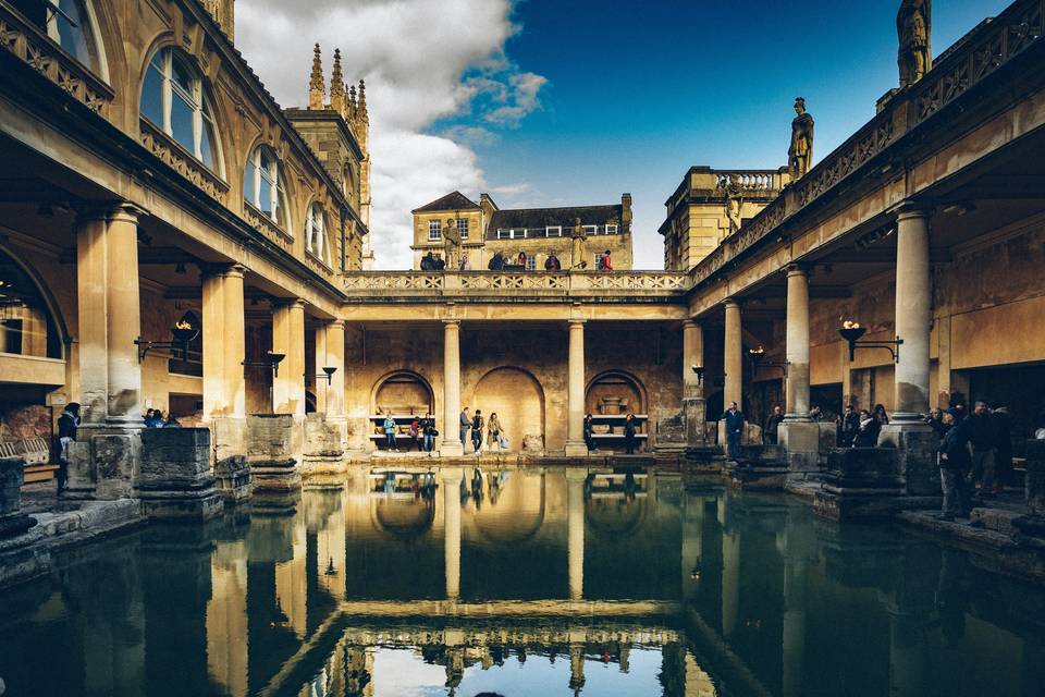 A picture of cool Bath hen do spot The Roman Baths showcasing the historical building with people walking around