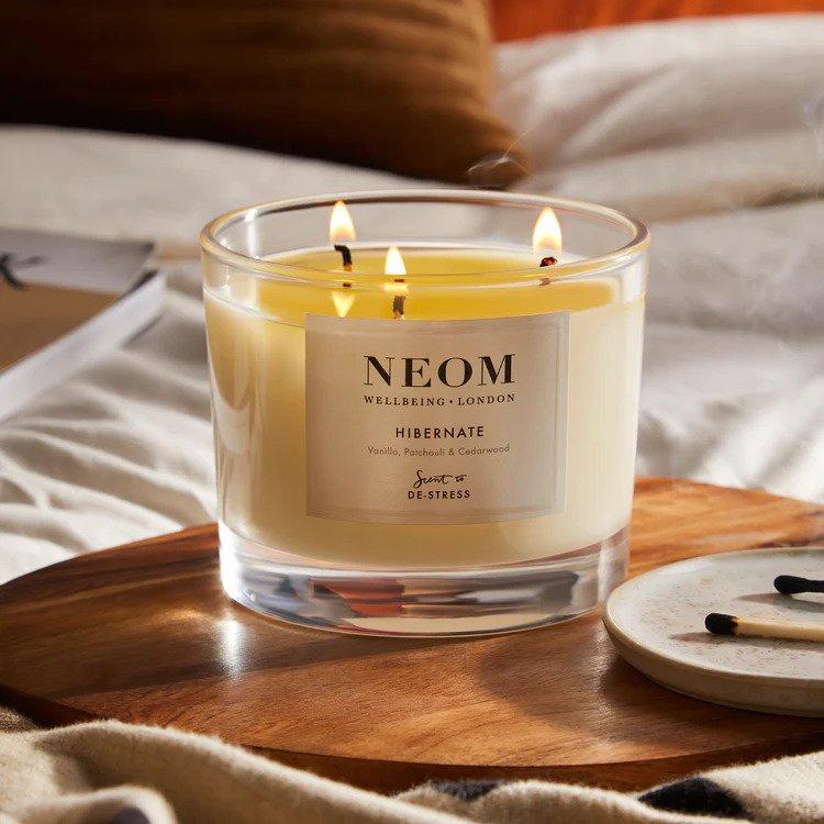 A three wick Neom candle with all wicks lit on a table