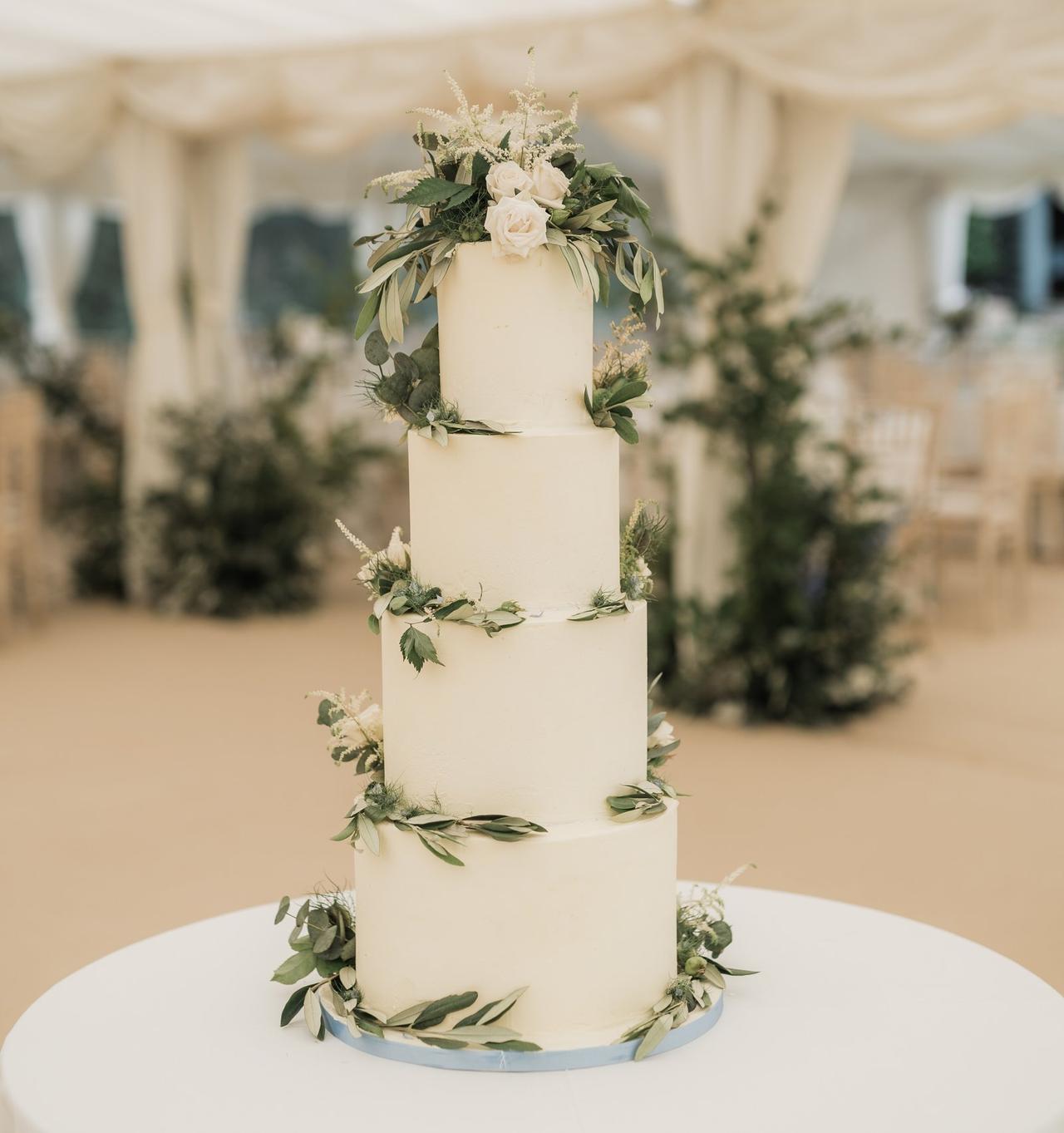 A tall white tiered wedding cake with greenery around each tier.