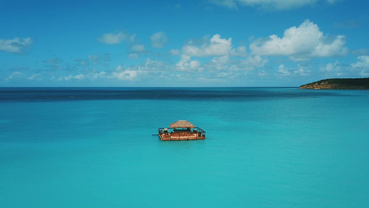 Bright blue ocean waters sit below a pastel blue sky with just one boat house sailing off into the ocean