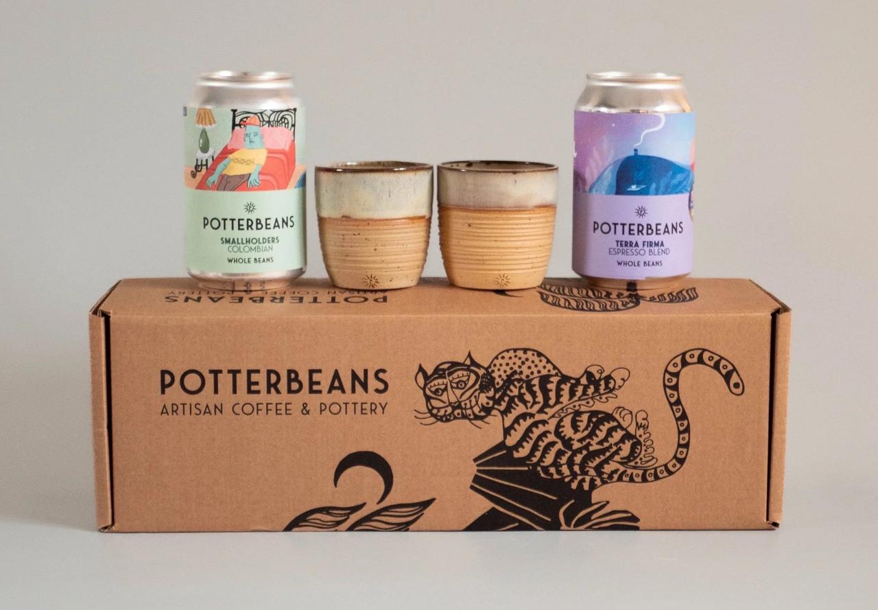 Two clay espresso cups and two tins of coffee atop a gift box