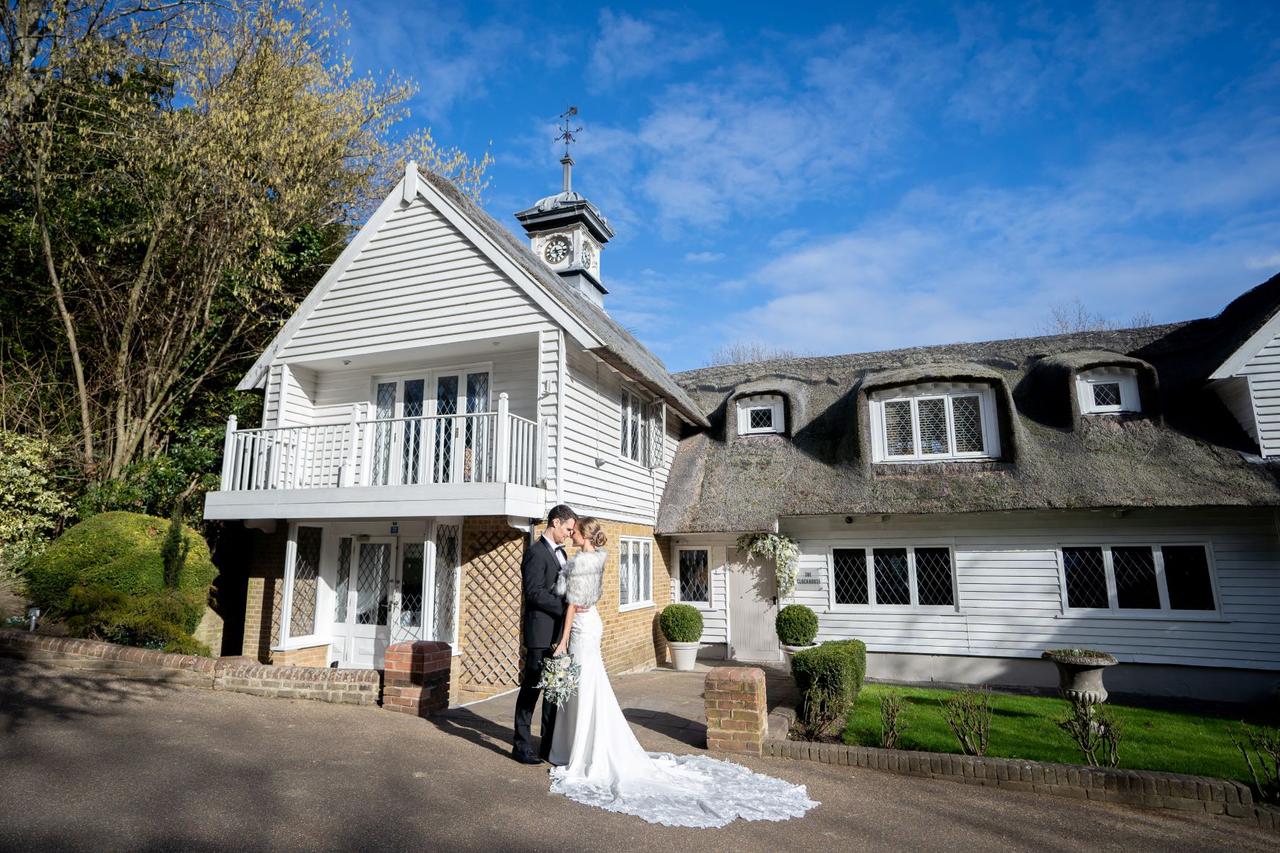 Bride and groom kissing outside of a wedding venue with wooden siding, a thatched roof and a balcony
