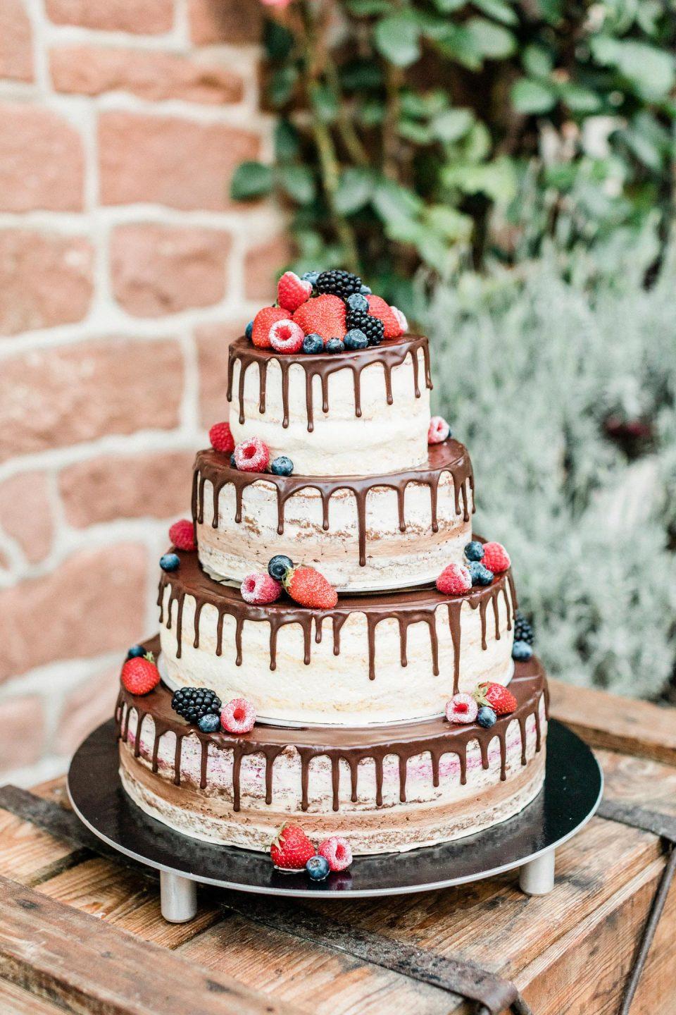 Four tiered rustic wedding cake with chocolate drips and berries