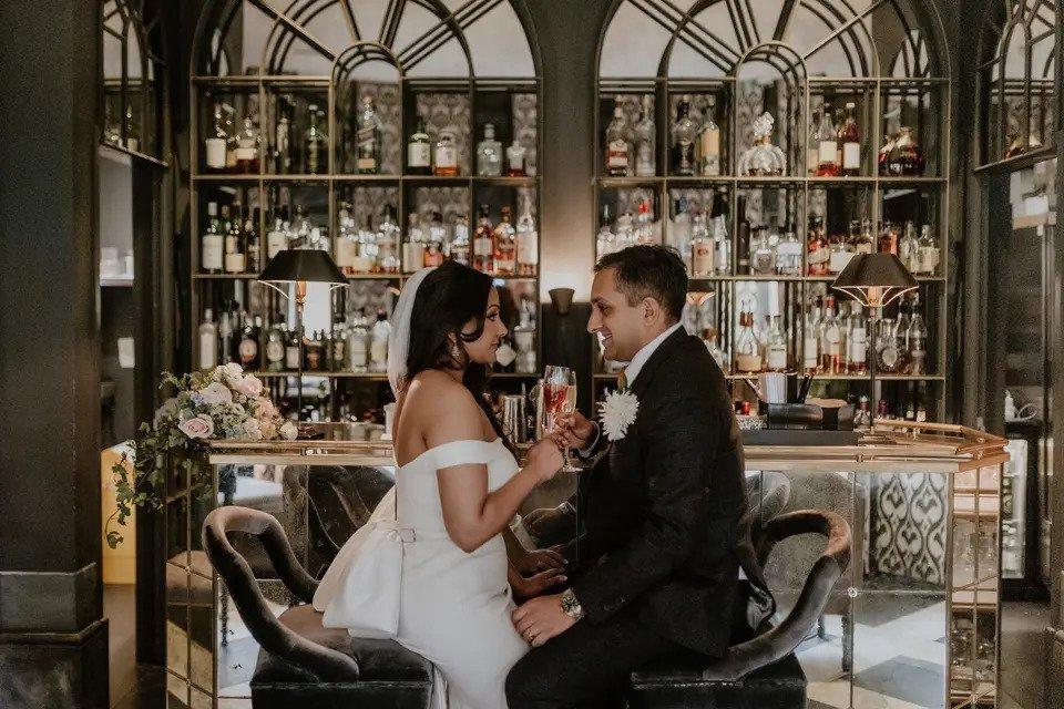Bride and groom sit facing each other in front of a bar