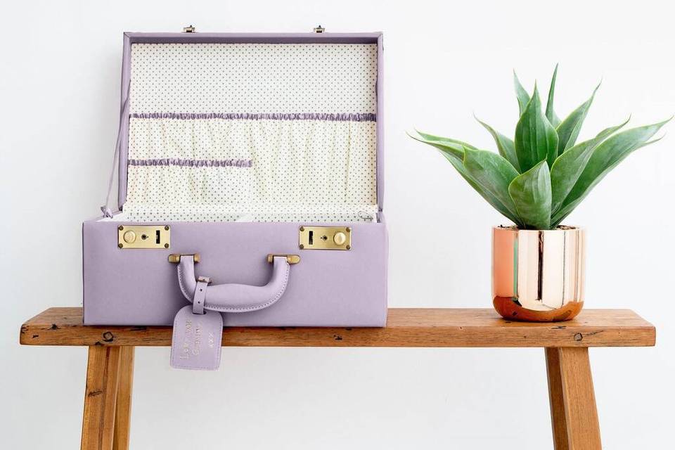 Lilac leather briefcase on a wooden table next to a plant in a copper pot