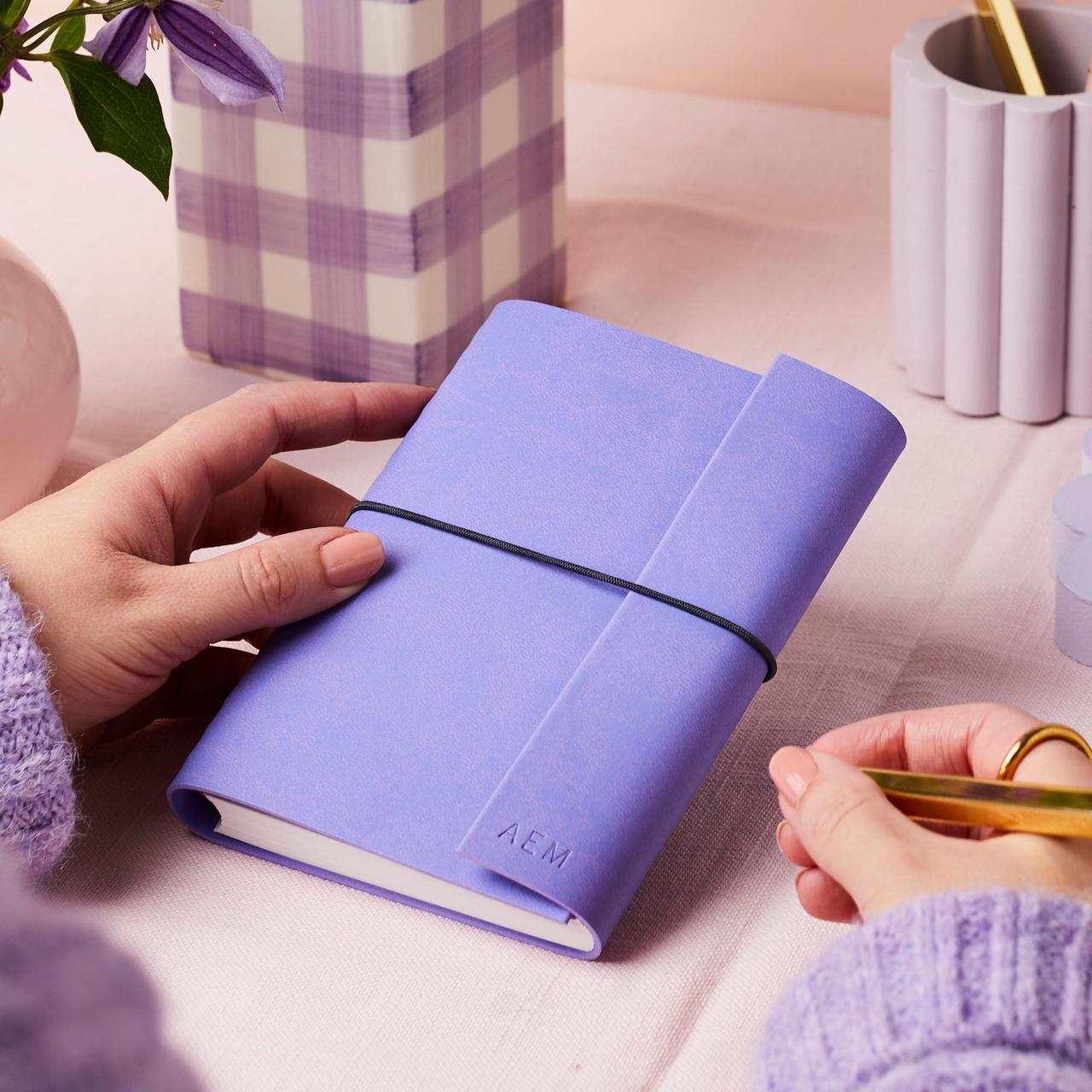 A woman holding a purple embossed vegan leather notebook and a gold pen.