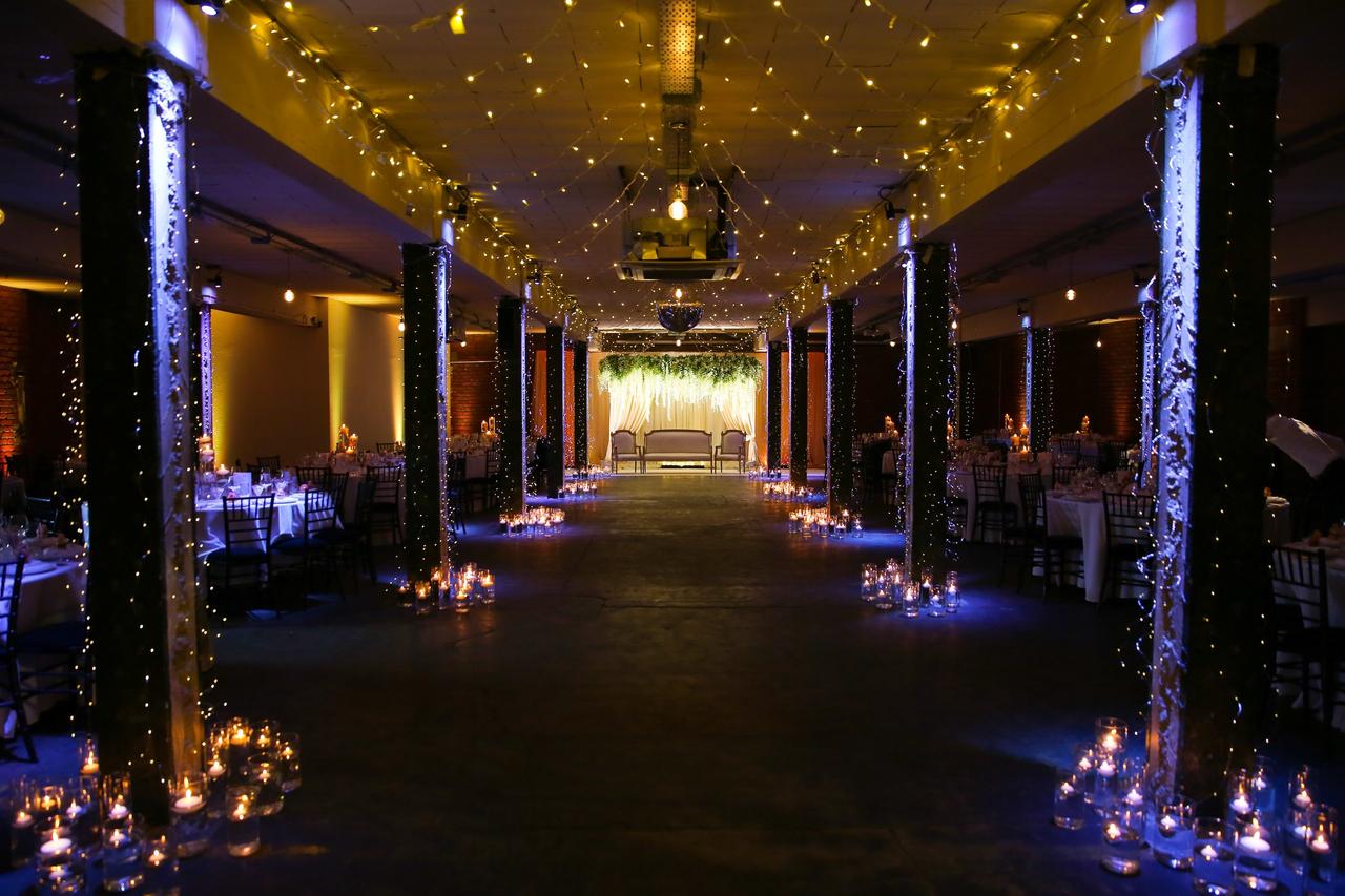 Interior of an industrial wedding venue set up for an Asian wedding with industrial pillars and exposed brickwork and lots of candles.