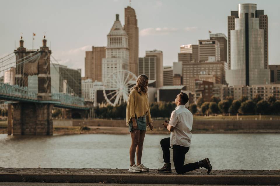 Man proposing to woman with the view of a city-scape and bride behind them