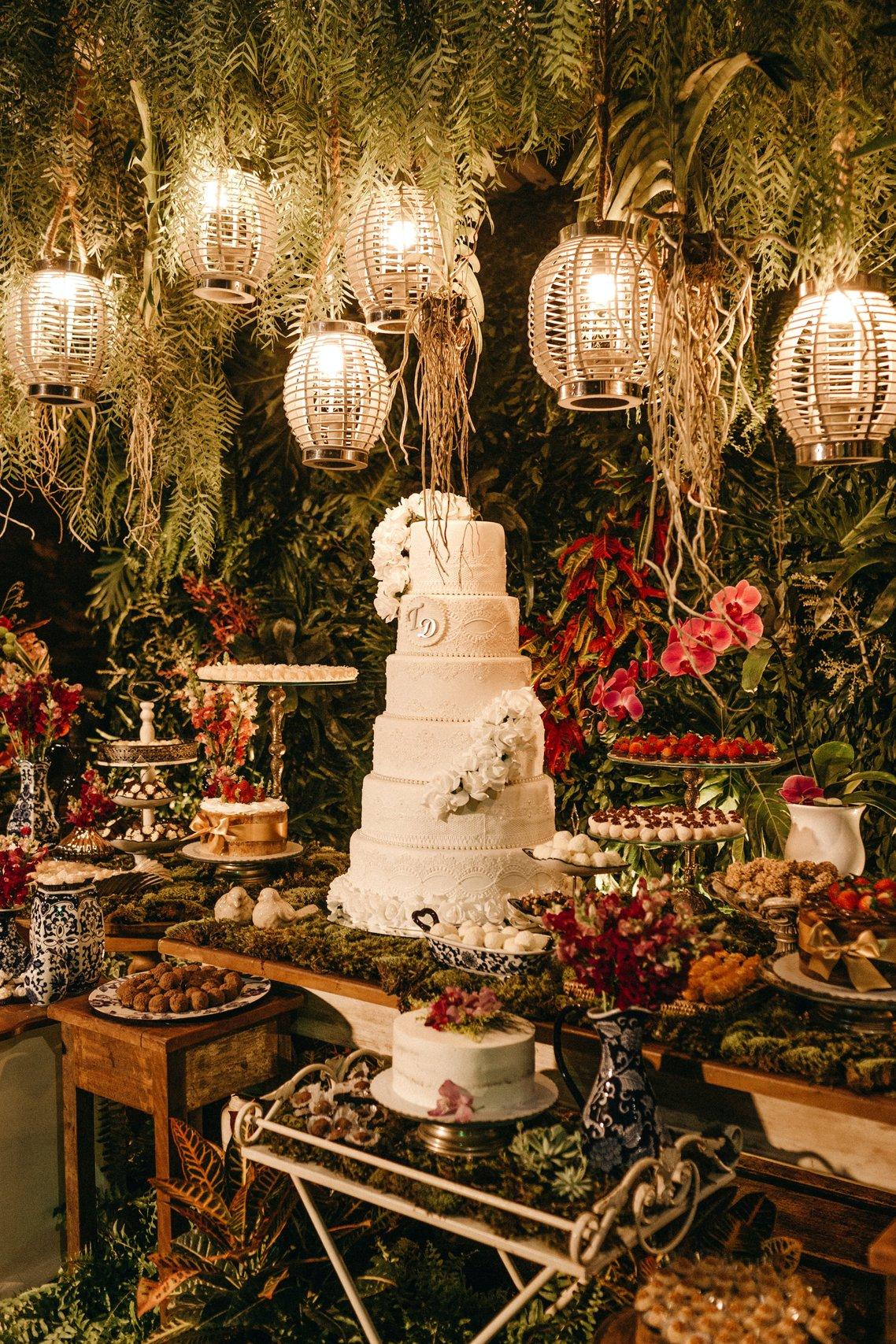 A lavish wedding cake and food table with hanging botanical garlands