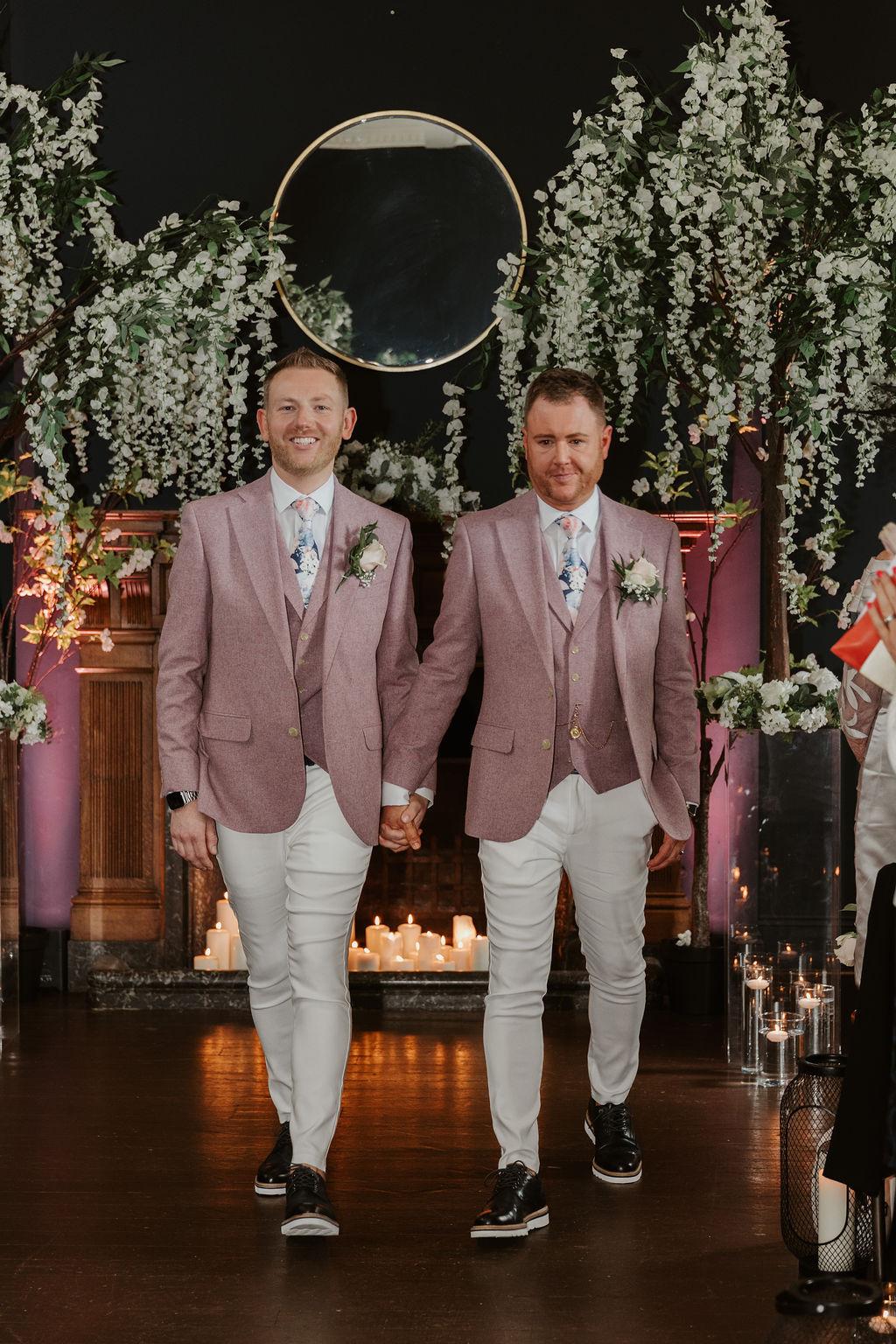 two grooms hold hands and walk down the aisle after tying the knot