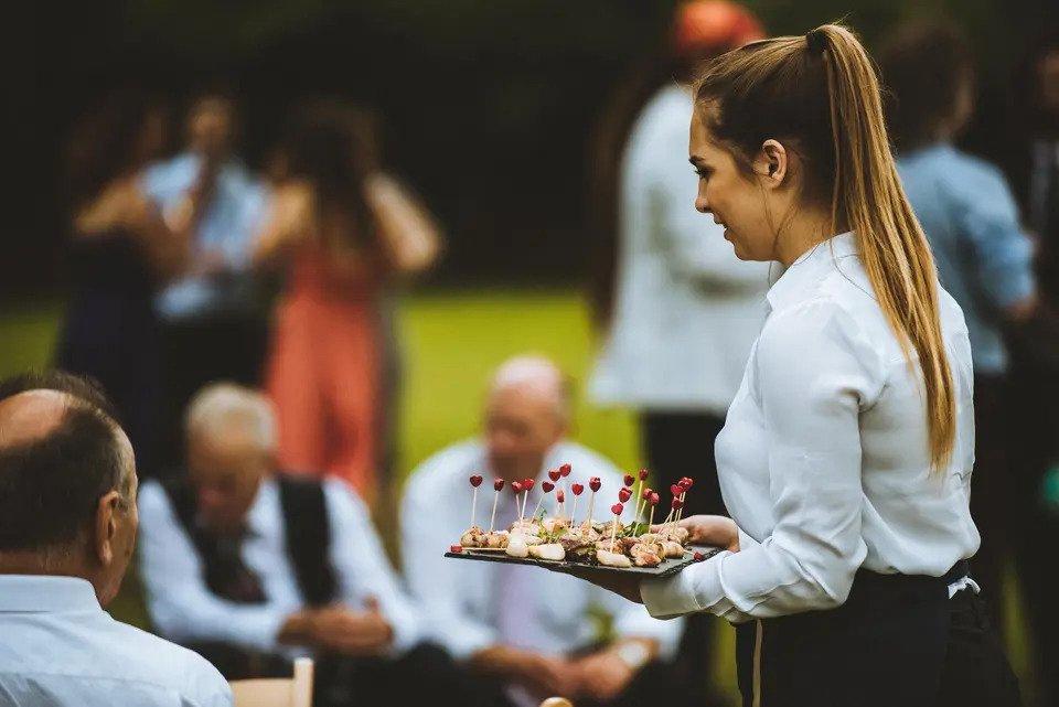 A waitress serves canapes to guests seated and standing outdoors
