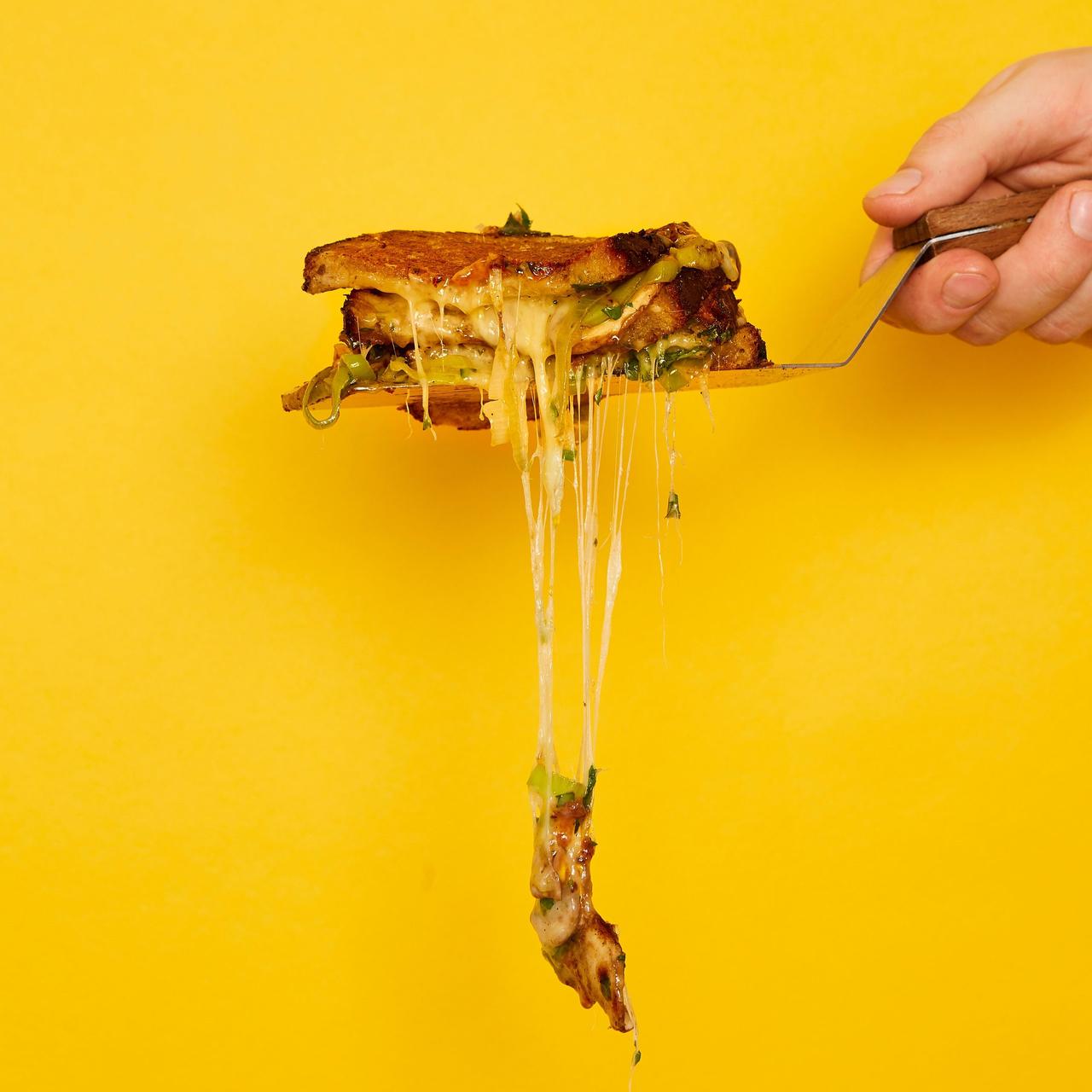 gooey grilled cheese on a spatula against a yellow background
