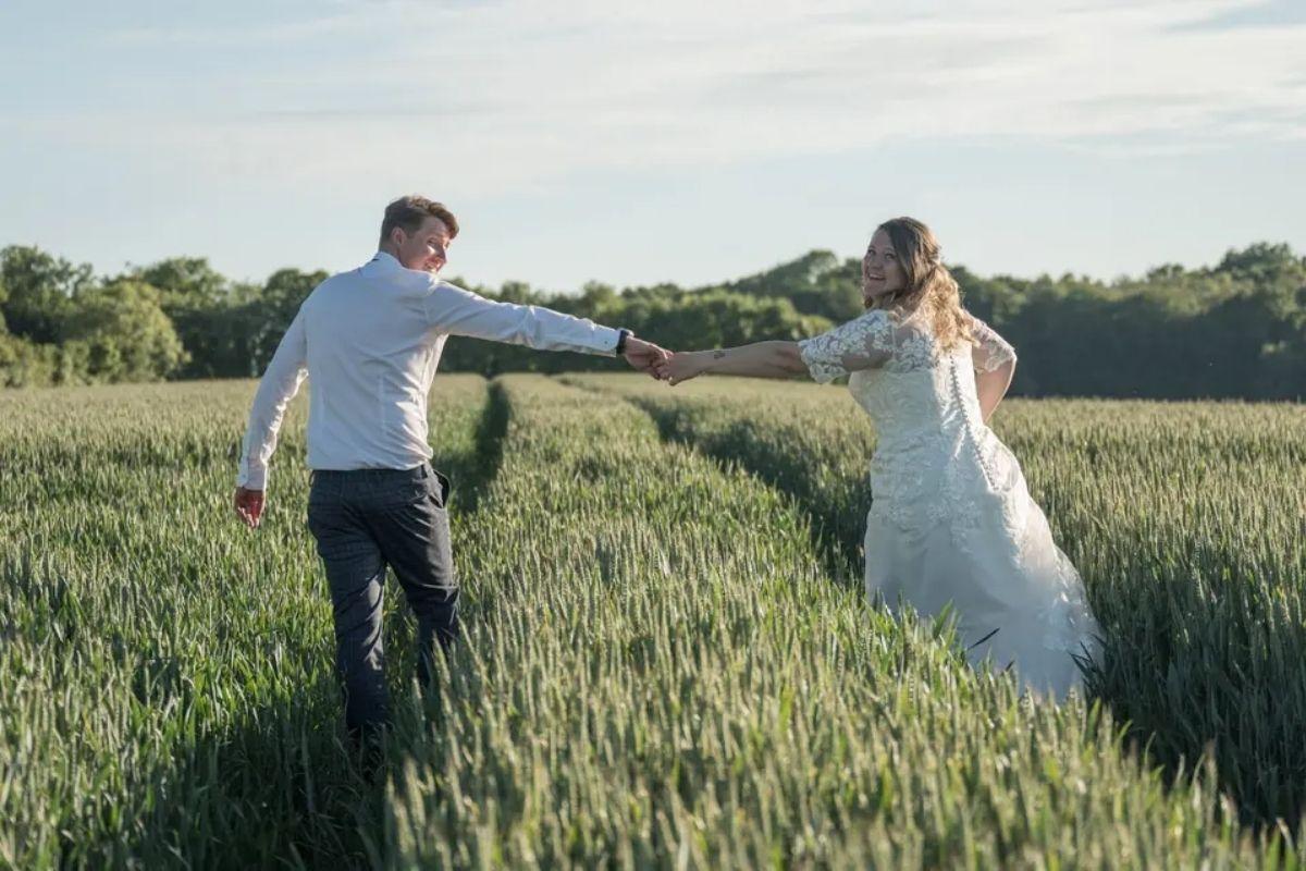 a bride and groom walking through a field reaching for each other's hands on their wedding day