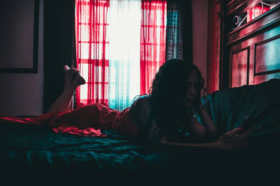 A woman lying on her bed in a dark room sending a sexy text message