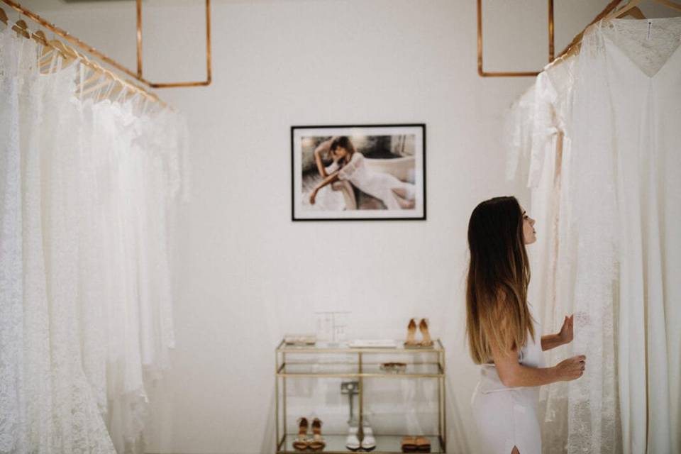 A female stylist looks at rows of wedding dresses hanging from racks in the Grace Loves Lace London showroom