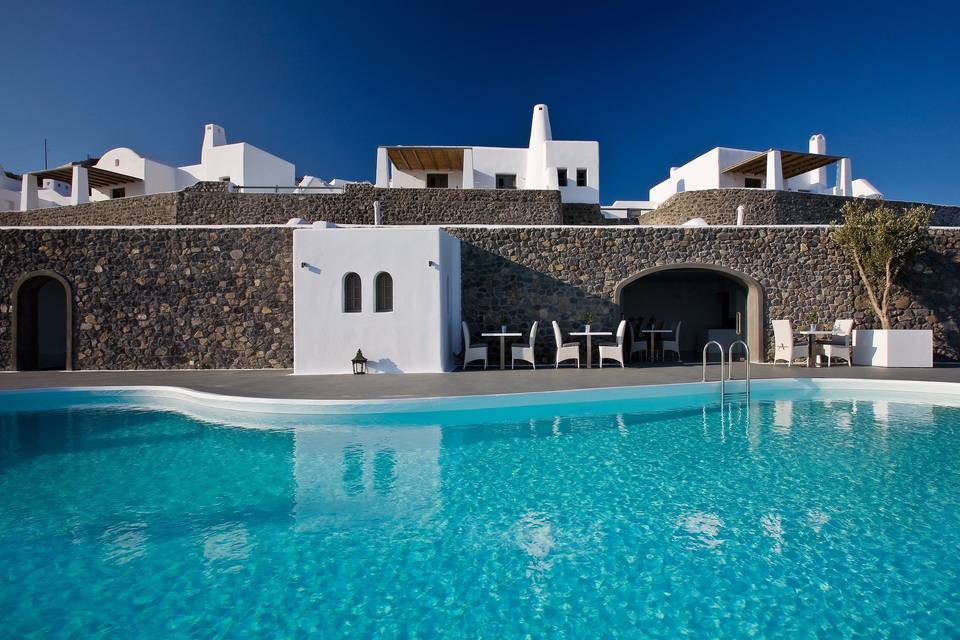Blue inifinity pool in front of a stone walled restaurant and upper floor with individual villas