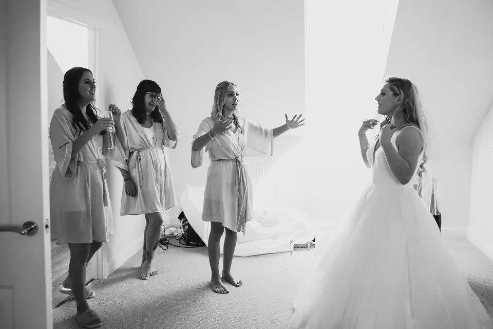 A black and white photo of three bridesmaids in their dressing gowns emotionally looking at a bride in her wedding dress
