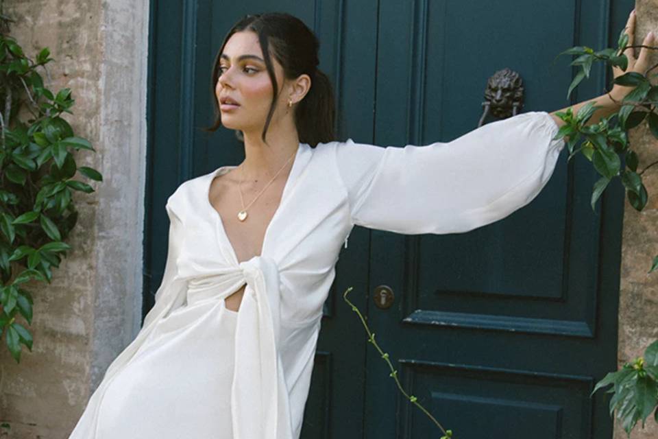 model wears tie front online wedding dress with long sleeves and stands in front of a navy door outside
